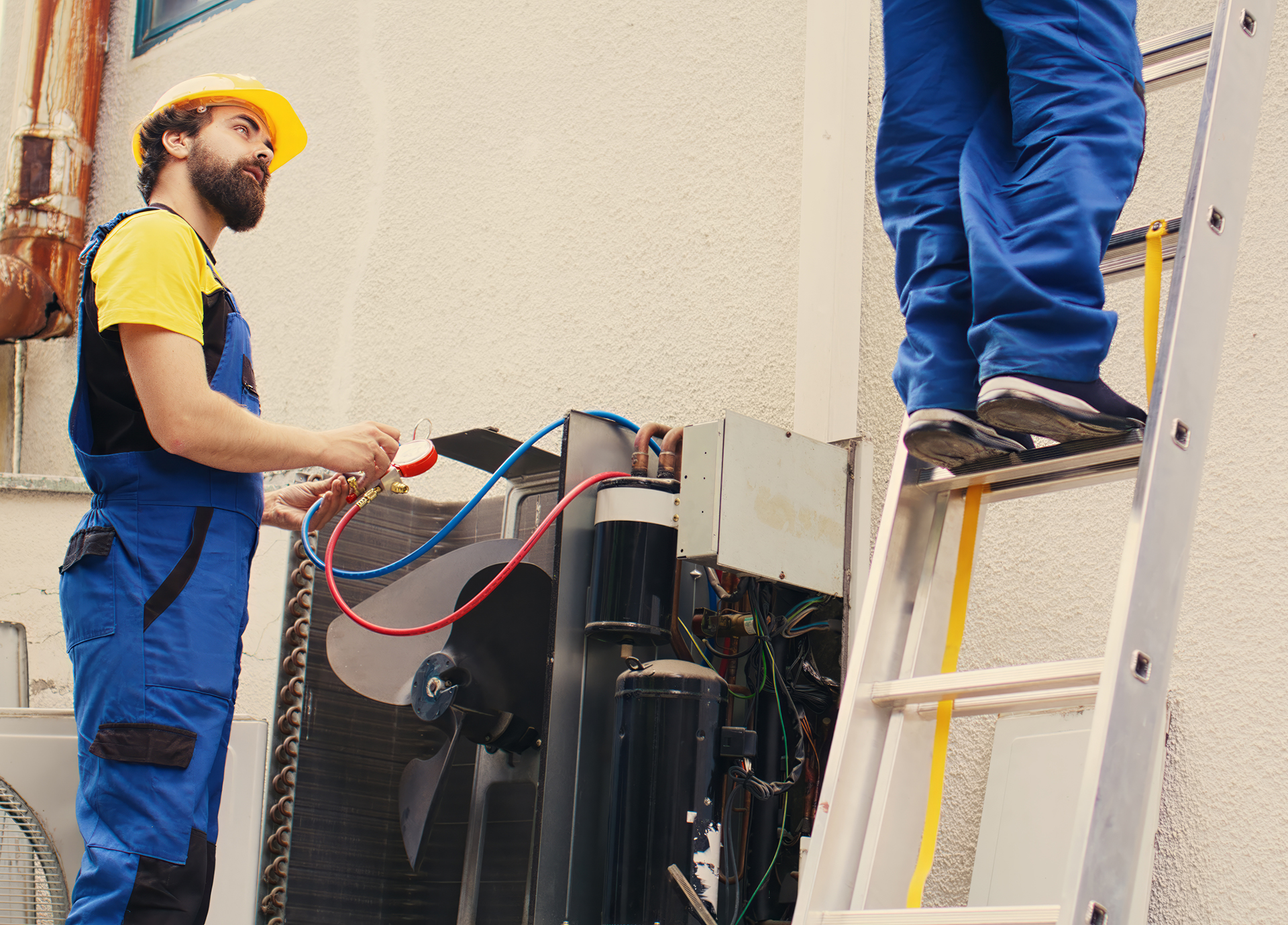 Proficient expert holding electric power drill stepping down from folding ladder after finishing servicing rooftop hvac system while coworker assembles manifold gauges to check freon levels